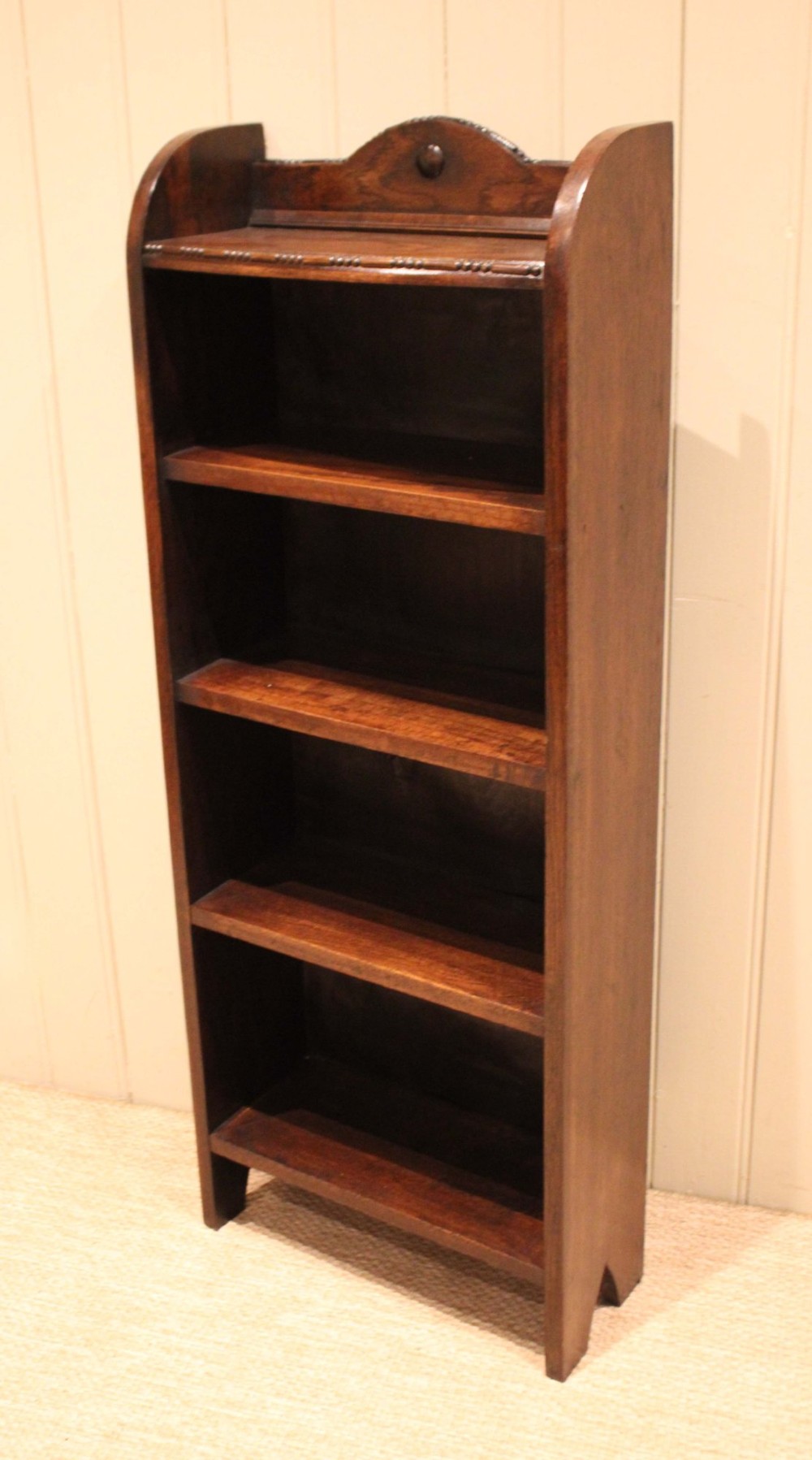 A slim freestanding dark oak open bookcase featuring four shelves and a shaped decorative pediment with a round motif. View VIII