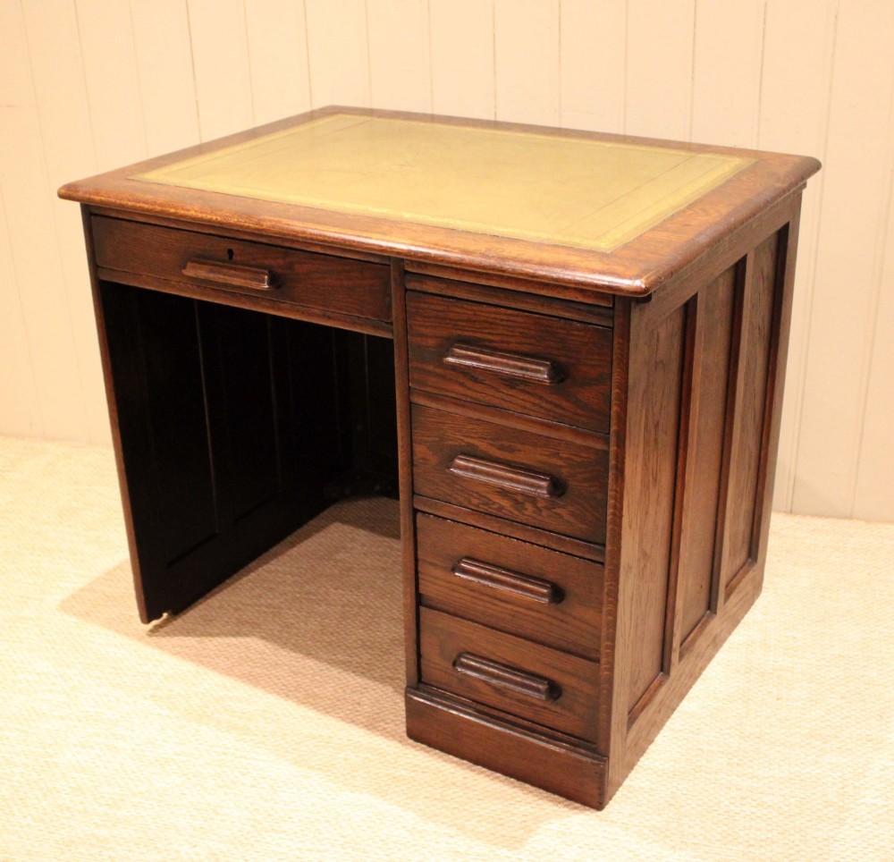 A small solid dark oak clerks desk featuring a leather inset writing surface, a single central drawer, and a four-drawer pedestal on the right. View II