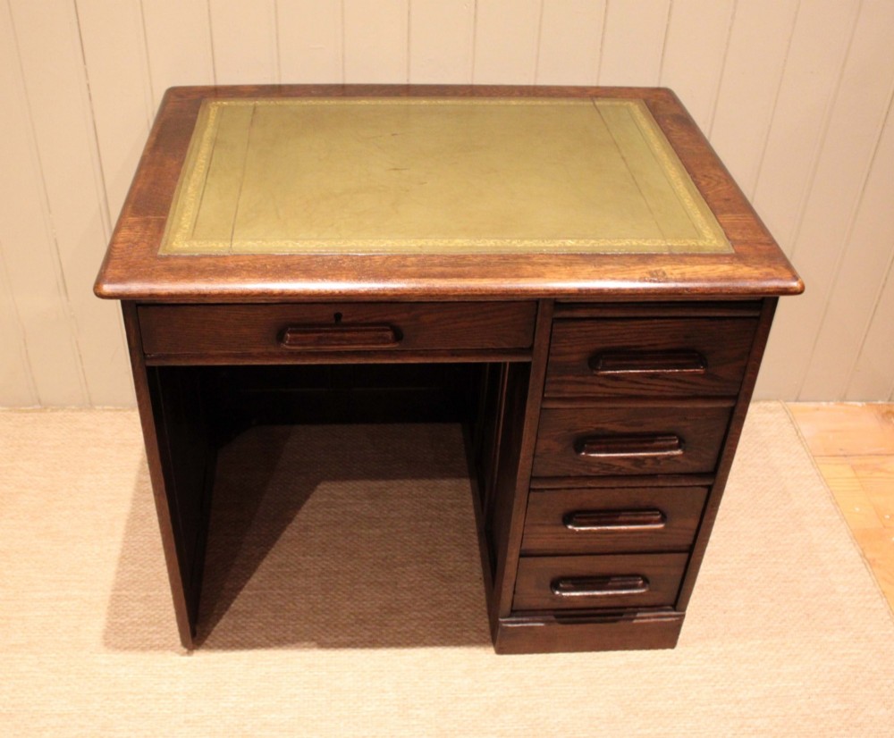 A small solid dark oak clerks desk featuring a leather inset writing surface, a single central drawer, and a four-drawer pedestal on the right. View III