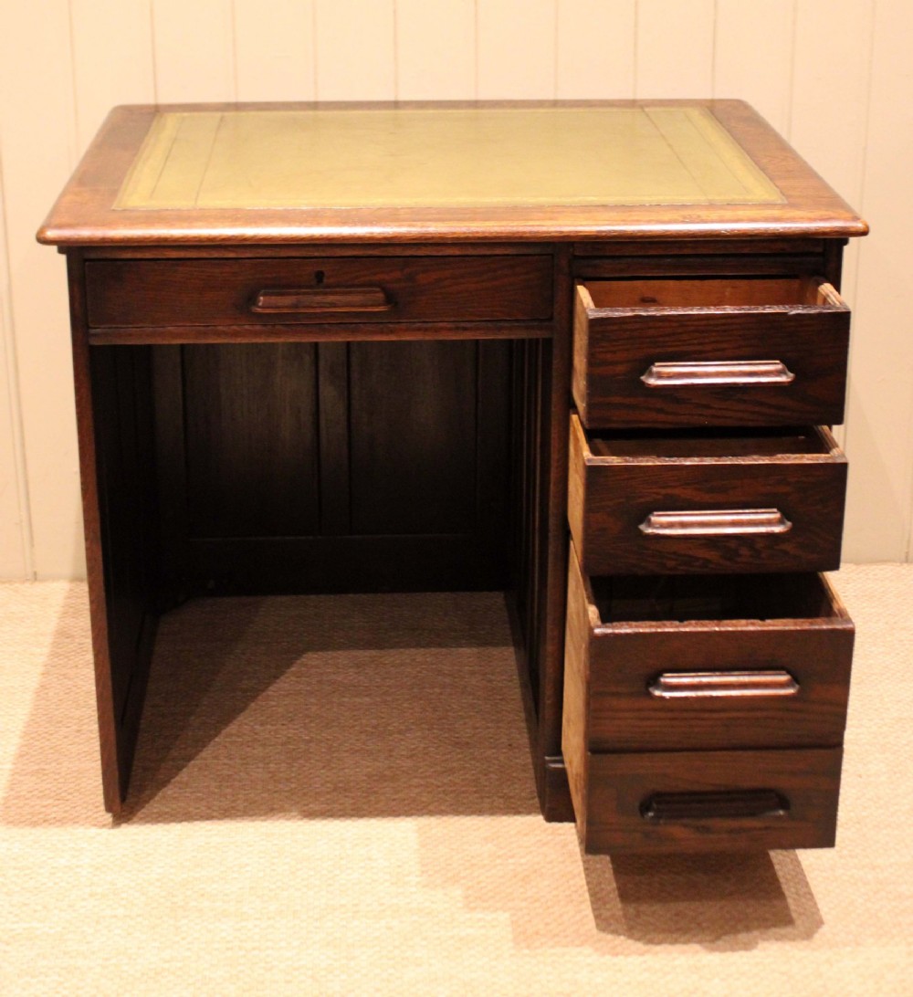 A small solid dark oak clerks desk featuring a leather inset writing surface, a single central drawer, and a four-drawer pedestal on the right. View IV