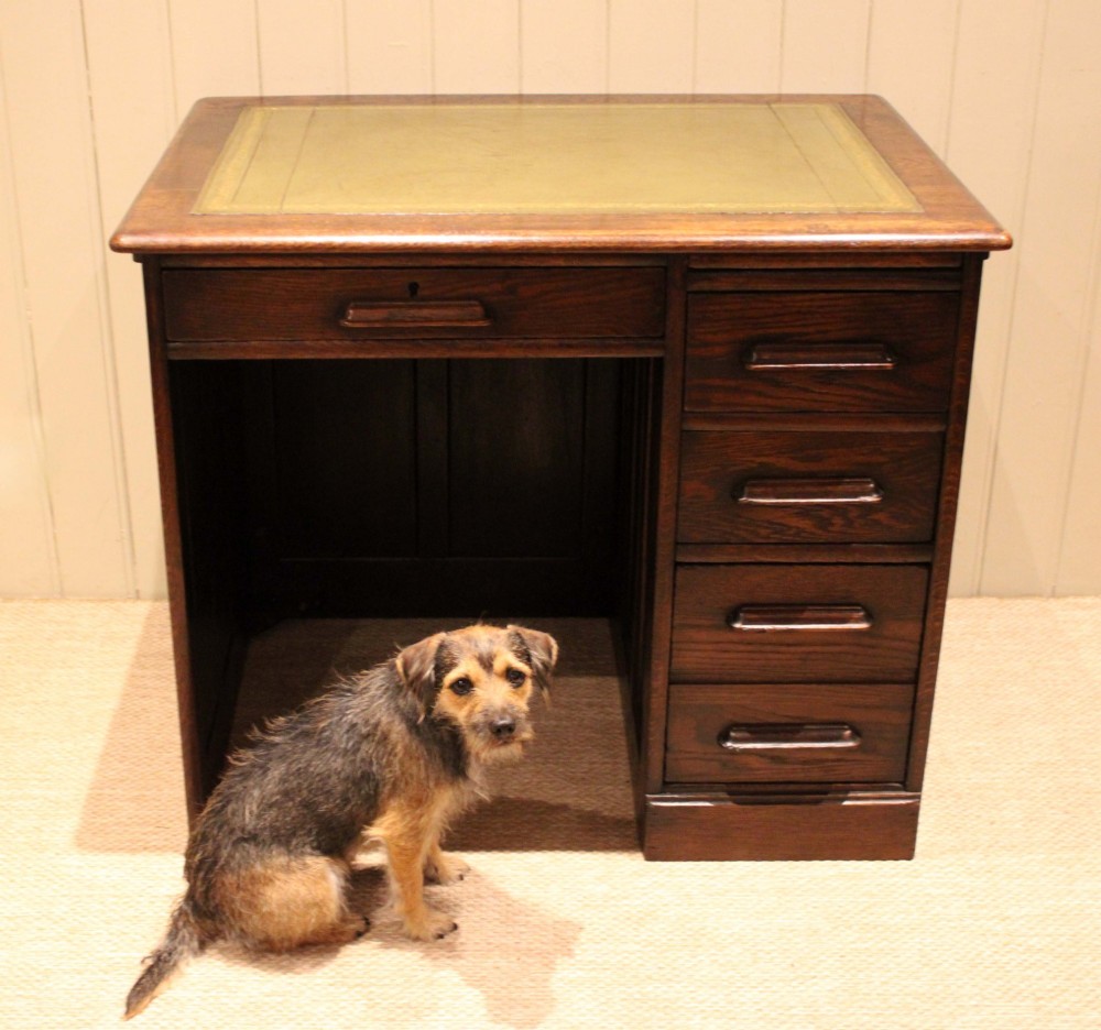A small solid dark oak clerks desk featuring a leather inset writing surface, a single central drawer, and a four-drawer pedestal on the right. View VI