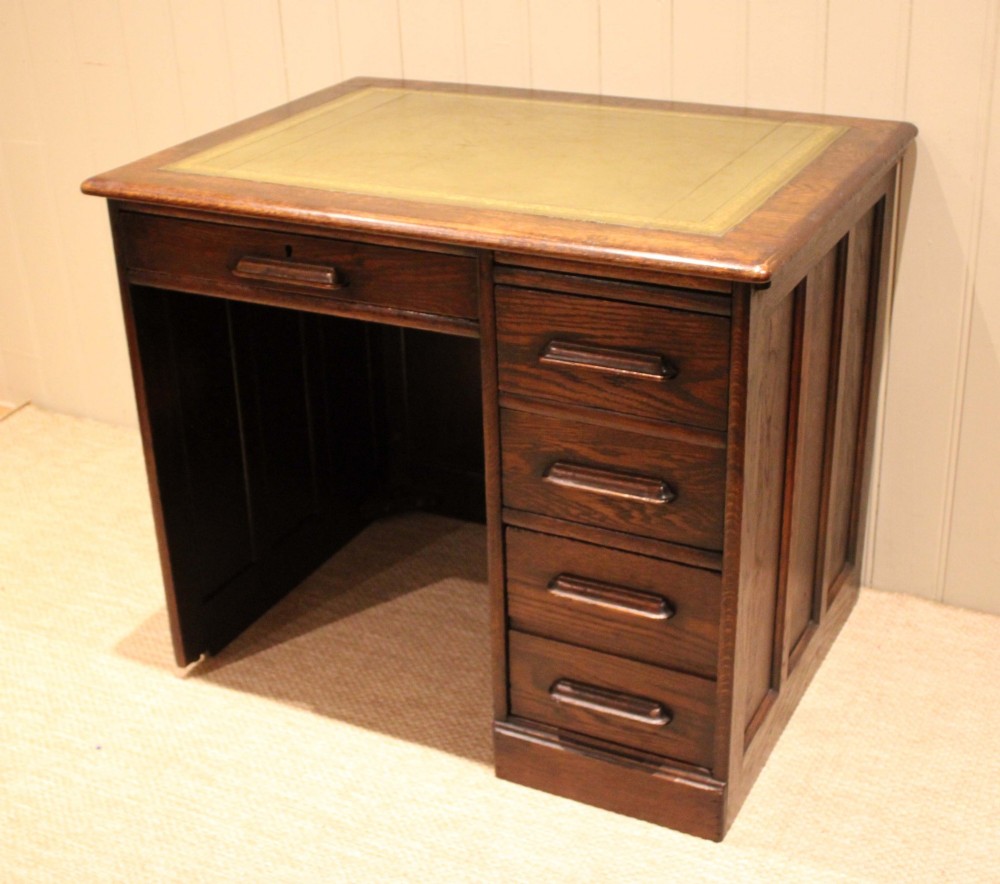 A small solid dark oak clerks desk featuring a leather inset writing surface, a single central drawer, and a four-drawer pedestal on the right. View VII