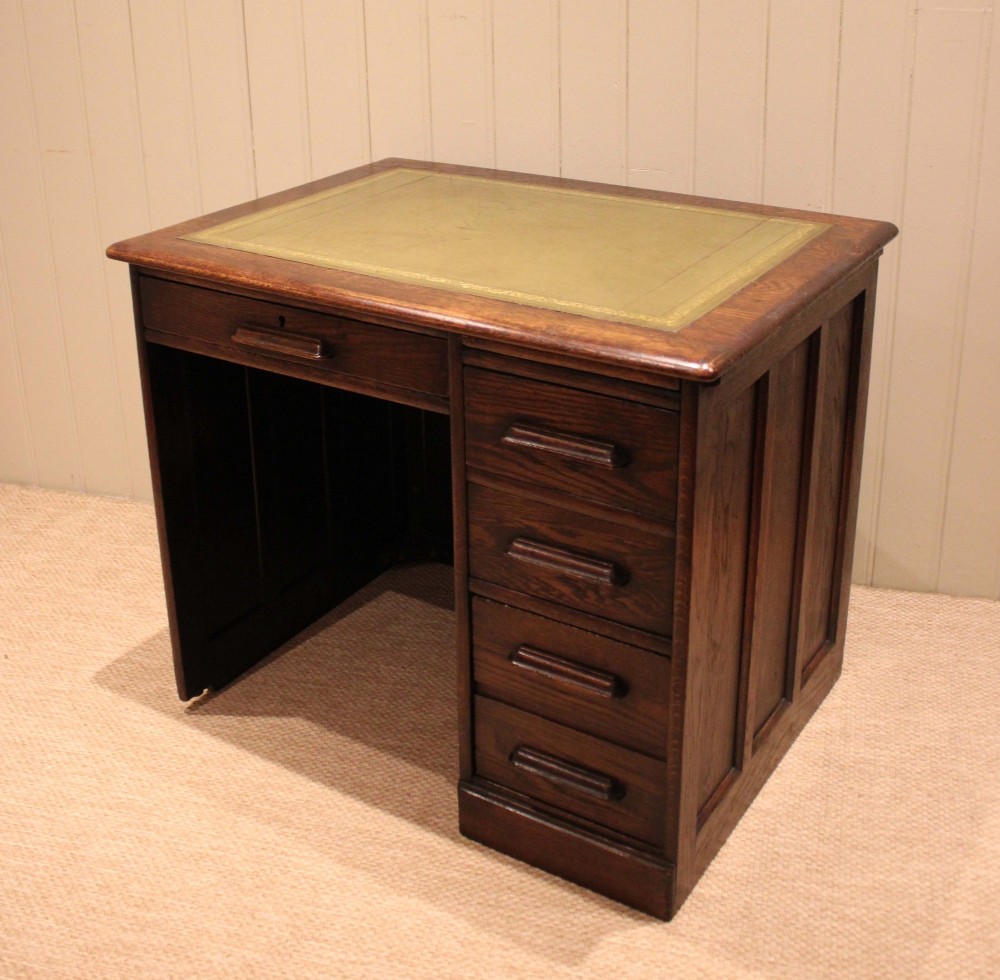 A small solid dark oak clerks desk featuring a leather inset writing surface, a single central drawer, and a four-drawer pedestal on the right. View VIII