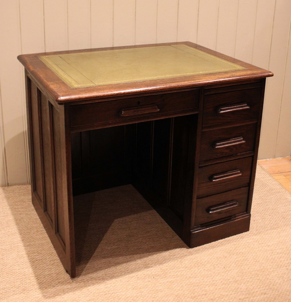 A small solid dark oak clerks desk featuring a leather inset writing surface, a single central drawer, and a four-drawer pedestal on the right. View IX