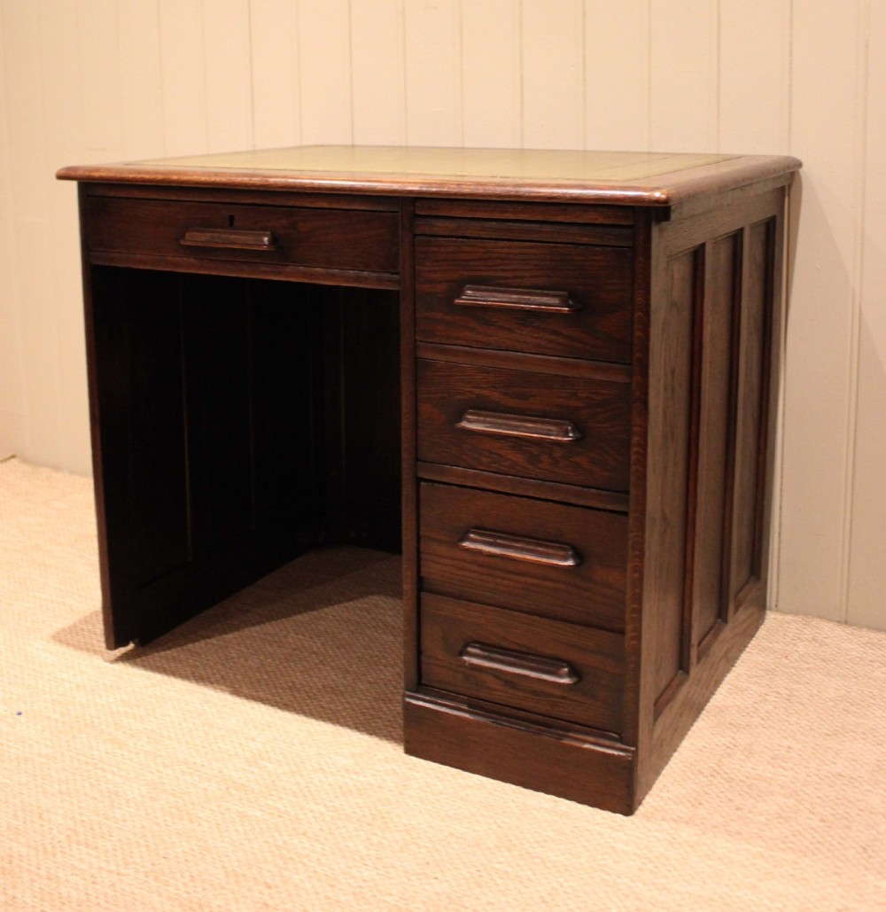 A small solid dark oak clerks desk featuring a leather inset writing surface, a single central drawer, and a four-drawer pedestal on the right. View X