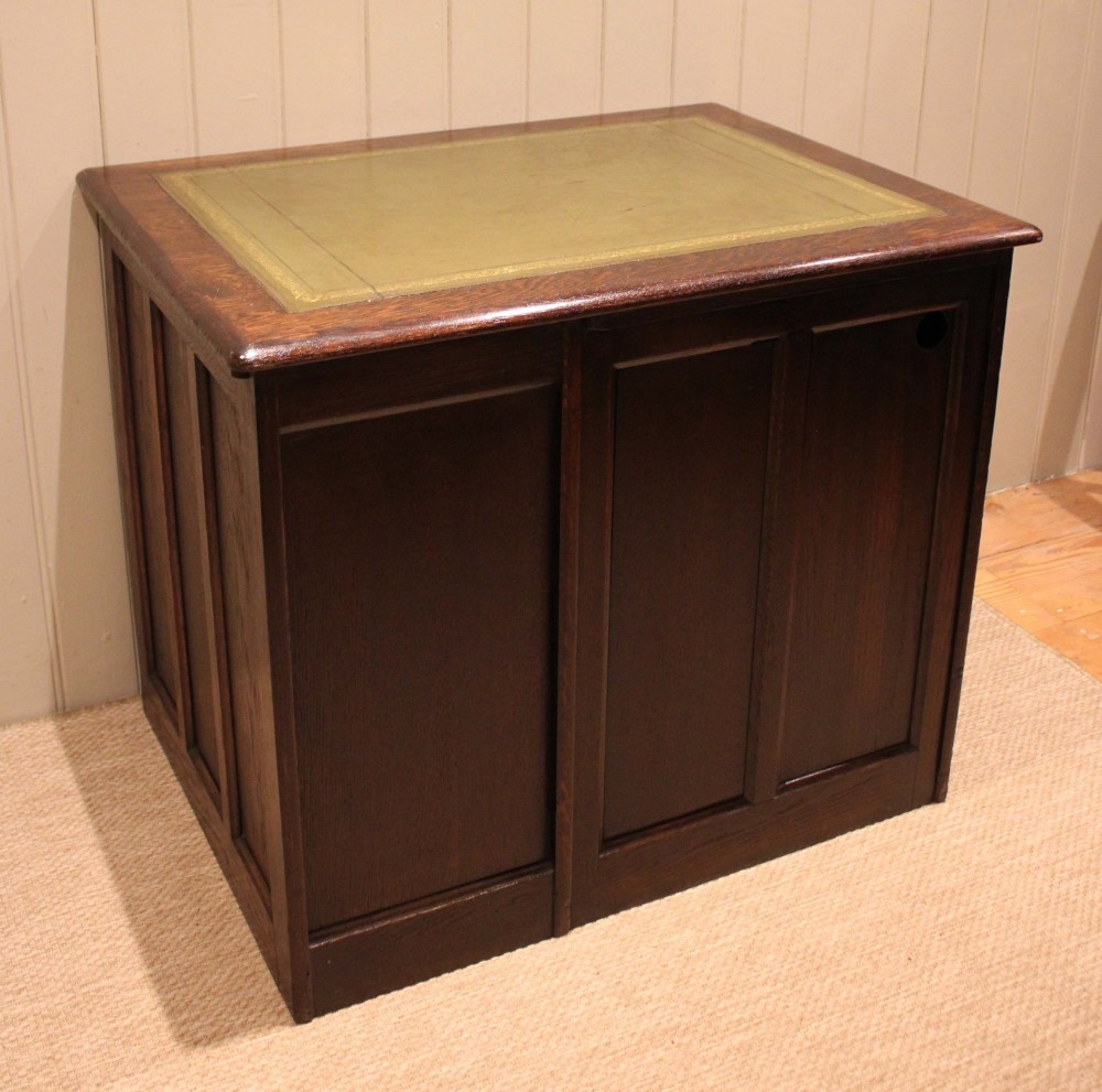A small solid dark oak clerks desk featuring a leather inset writing surface, a single central drawer, and a four-drawer pedestal on the right. View XI