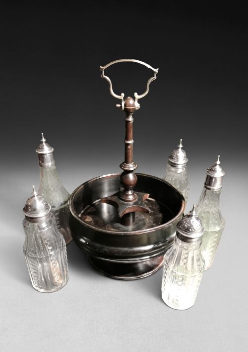 fig 1. An ebonised wooden circular cruet stand holding five cut glass bottles with fitted silver caps and a central carrying handle.