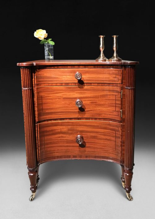 fig 1. A Regency mahogany concave-fronted commode featuring three drawers, ebony line inlay, reeded side columns, turned legs, and brass castors.