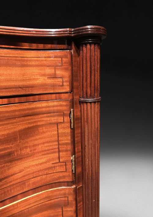 fig 4. A Regency mahogany concave-fronted commode featuring three drawers, ebony line inlay, reeded side columns, turned legs, and brass castors.