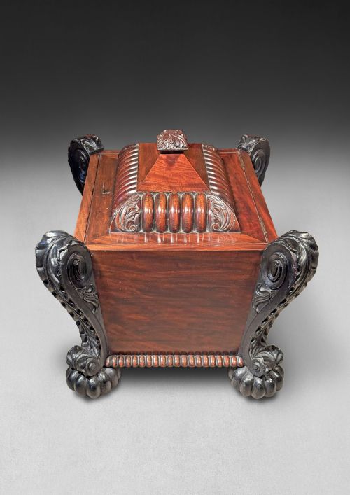 fig 1. A Regency mahogany and ebonised cellarette featuring a sarcophagus-form hinged lid with carved gadrooning, set on heavy scroll corner feet.