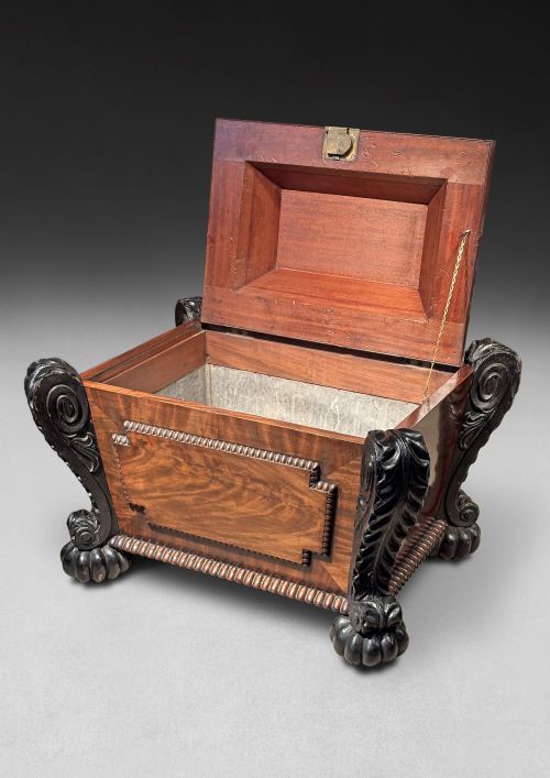 fig 4. A Regency mahogany and ebonised cellarette featuring a sarcophagus-form hinged lid with carved gadrooning, set on heavy scroll corner feet.
