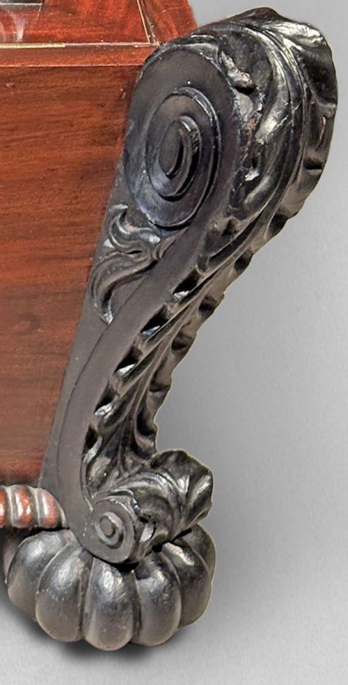 fig 5. A Regency mahogany and ebonised cellarette featuring a sarcophagus-form hinged lid with carved gadrooning, set on heavy scroll corner feet.