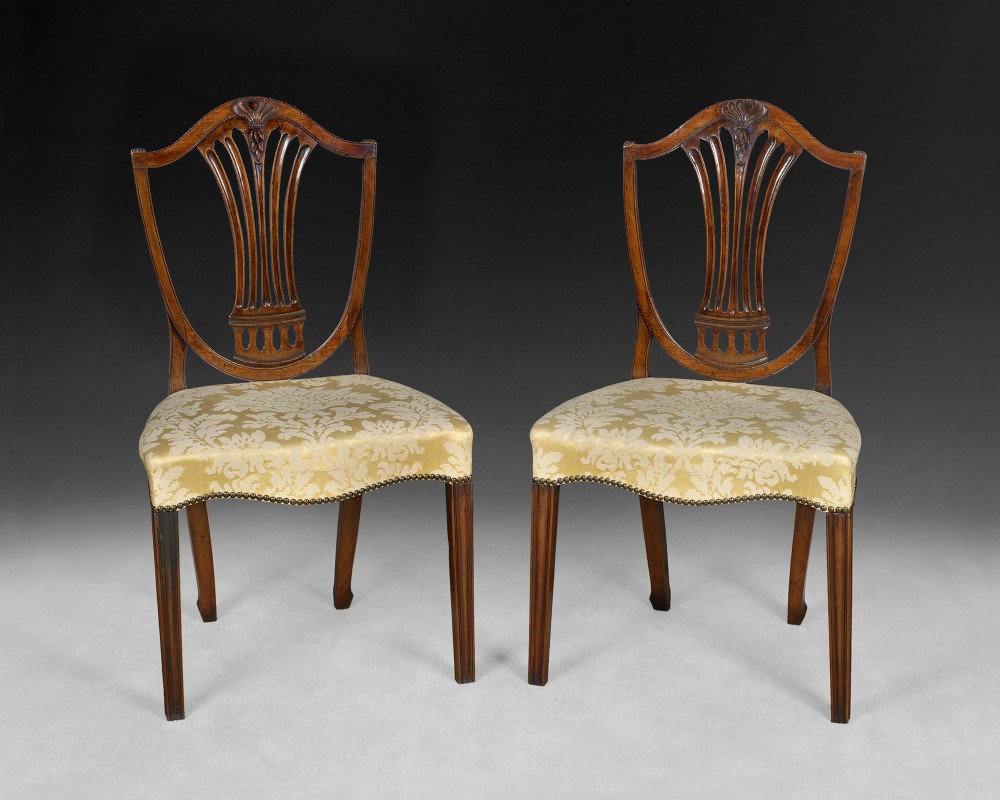 A pair of Hepplewhite Period Mahogany shield back side chairs with anthemion (honeysuckle) carved detail