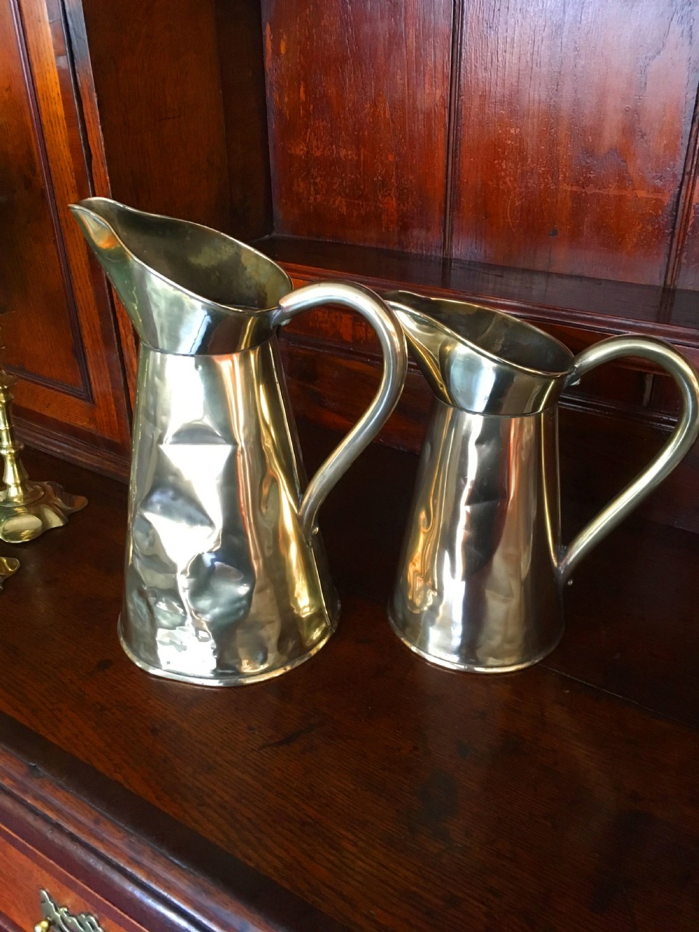 A pair of polished Victorian brass jugs featuring tapered bodies, wide spouts, and curved loop handles. View II