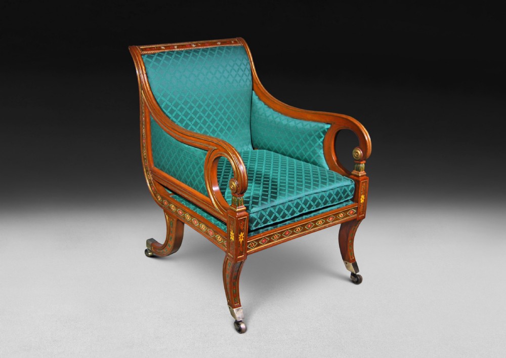 A Regency period library armchair constructed from painted and gilt-simulated satinwood with scrolled arms, upholstered in patterned green fabric and supported on brass castors. View V