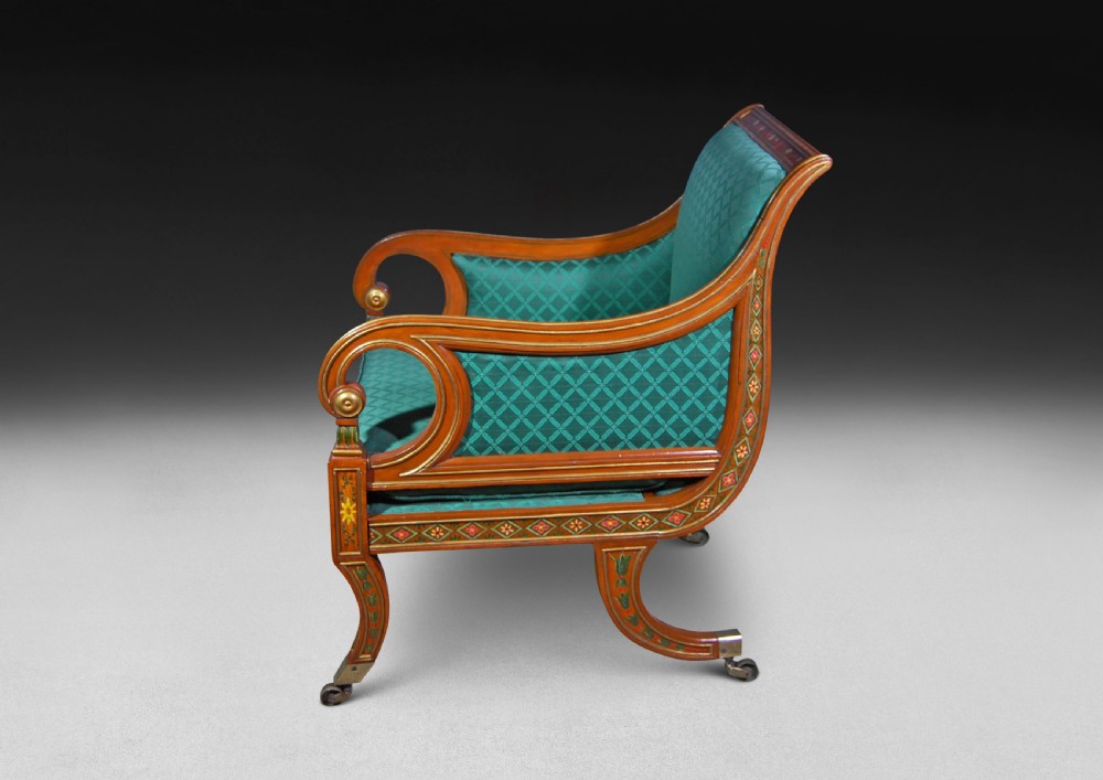 A Regency period library armchair constructed from painted and gilt-simulated satinwood with scrolled arms, upholstered in patterned green fabric and supported on brass castors. View III