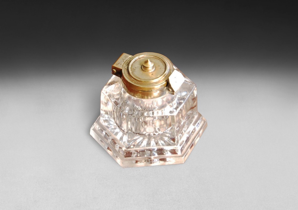 A heavy Victorian cut glass inkwell featuring a hexagonal faceted body and a hinged brass lid.