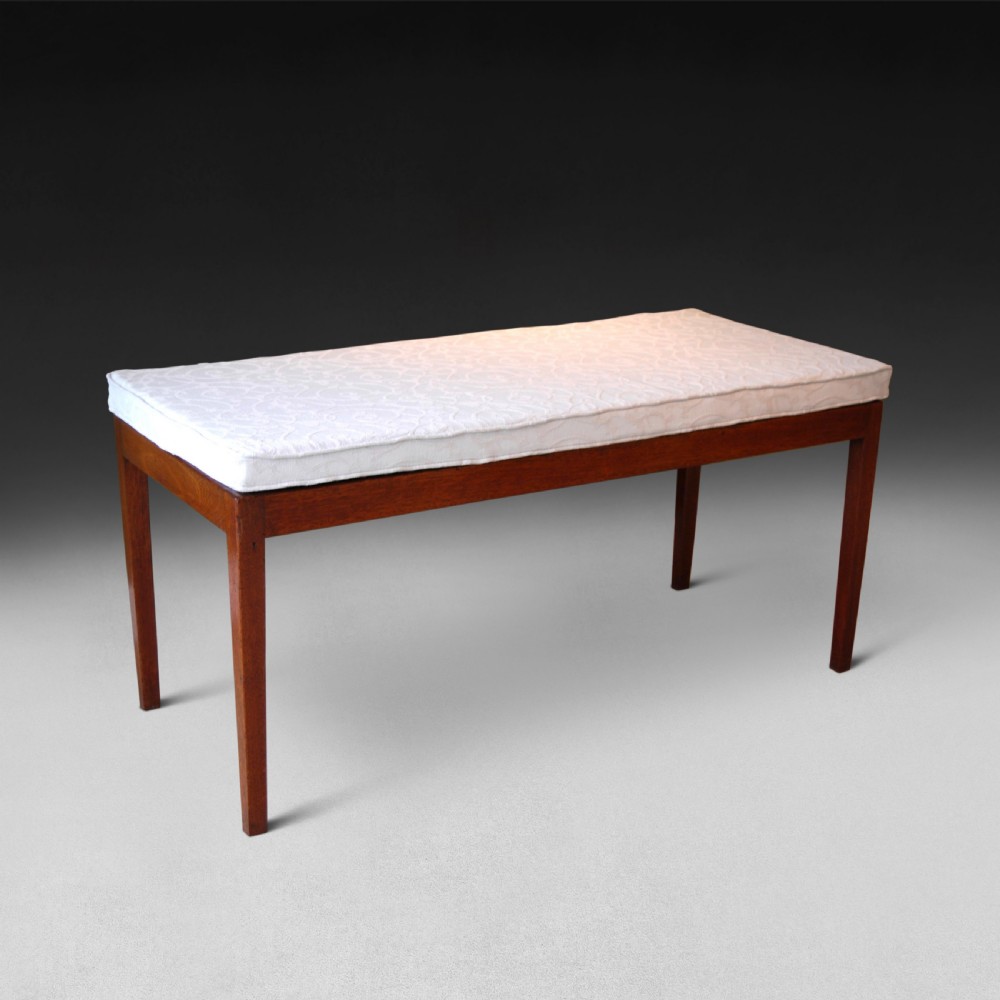 A George III period mahogany rectangular bed foot stand featuring four tapered square legs and a cream upholstered top cushion.