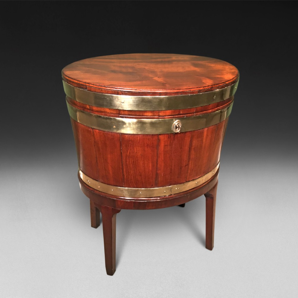 A George III period oval mahogany wine cooler on four tapered legs with polished brass structural bands and a fitted hinged lid.