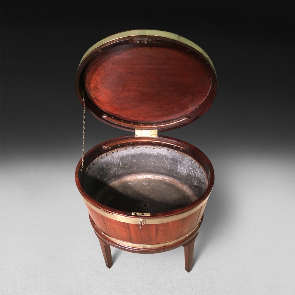 A George III period oval mahogany wine cooler on four tapered legs with polished brass structural bands and a fitted hinged lid. View II