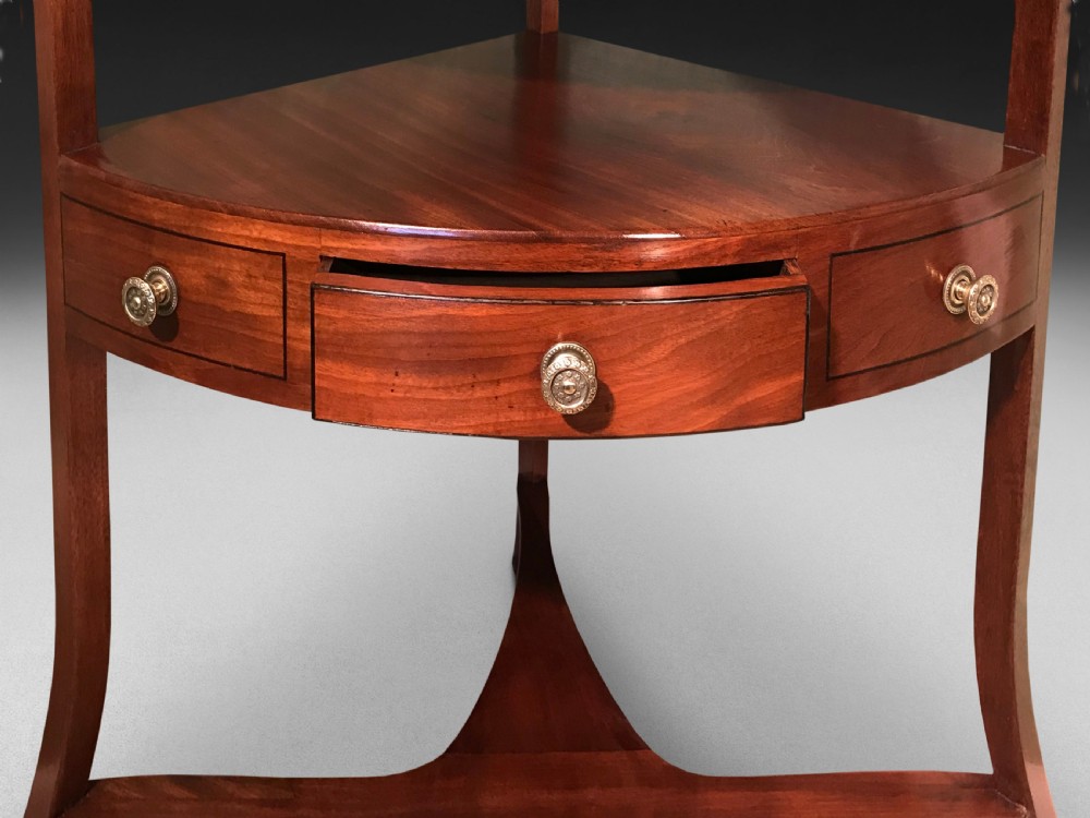 A George III mahogany corner washstand featuring a raised curved splashback, green leather top insert, lower drawer tier with brass pulls, and splayed legs. View IV