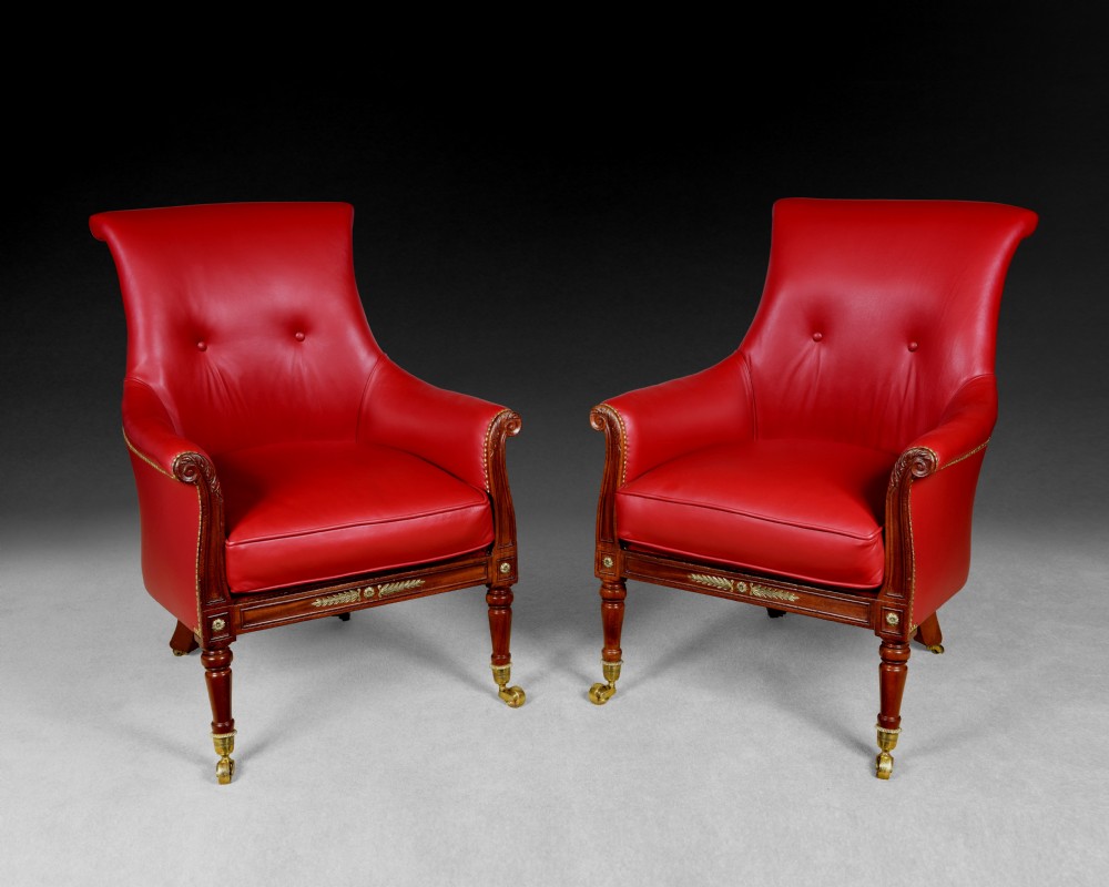A pair of Regency mahogany armchairs upholstered in bright red leather with turned front legs set on brass castors.