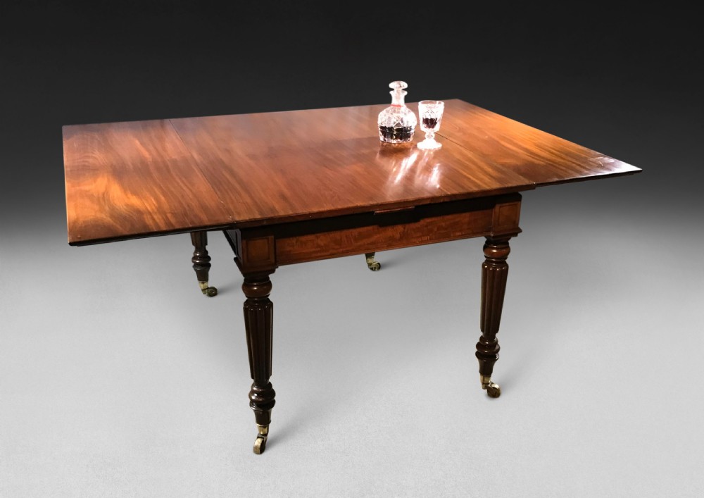 A Regency mahogany draw-leaf dining table with extended leaves, reeded legs, and brass cup castors.