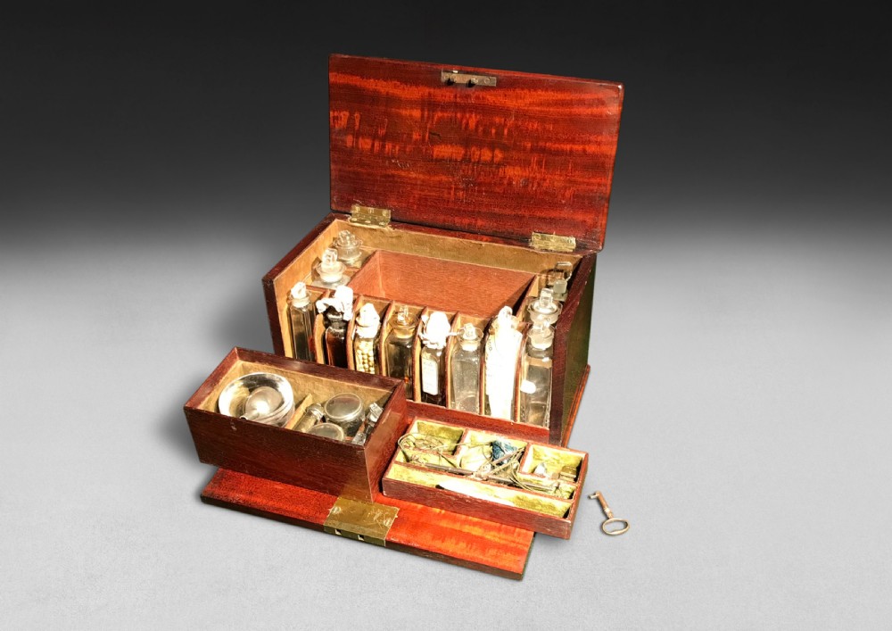 A Regency mahogany apothecary box shown open to display glass bottles, small drawers, brass fittings, and a key.