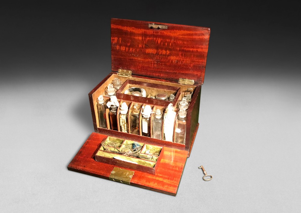 A Regency mahogany apothecary box shown open to display glass bottles, small drawers, brass fittings, and a key. View II