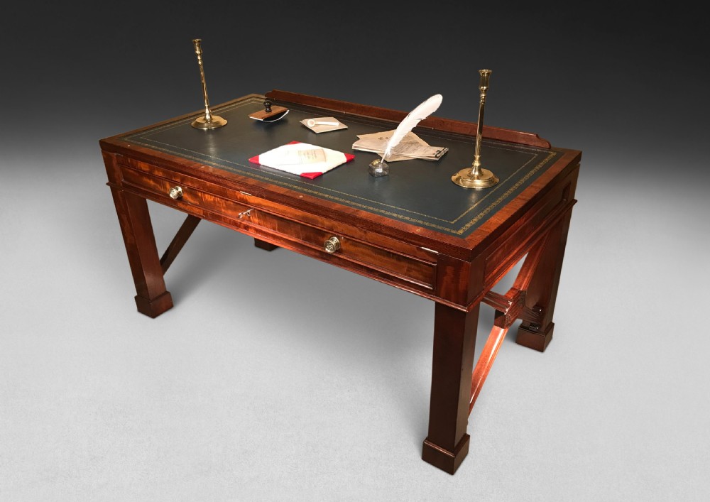 A Regency mahogany library table with a leather writing surface, a low rear gallery, a frieze drawer with brass knobs, and structured end supports.