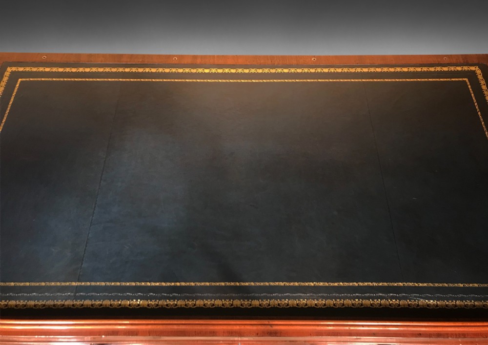 A Regency mahogany library table with a leather writing surface, a low rear gallery, a frieze drawer with brass knobs, and structured end supports. View X