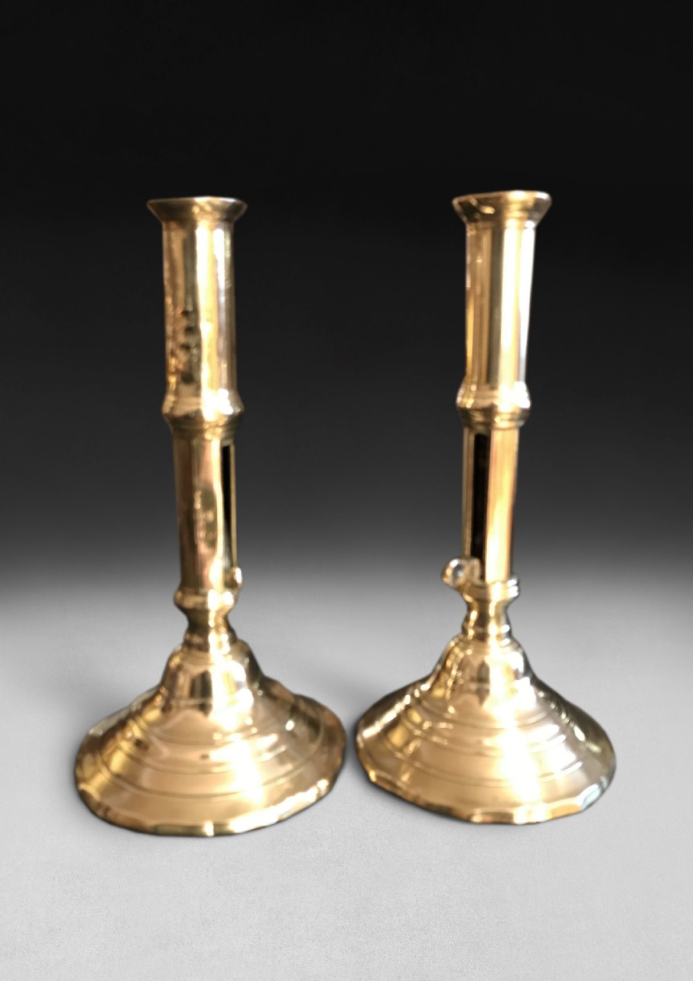 A pair of polished brass Georgian ejector candlesticks featuring turned stems, side sliding push-up levers, and flared circular bases.