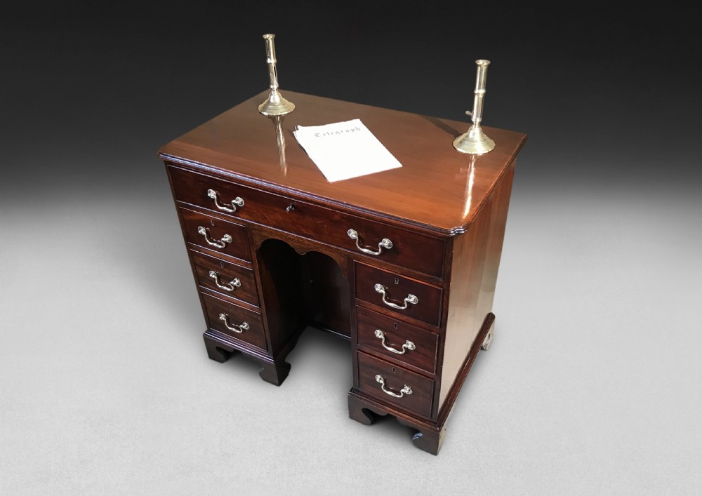 A George III dark mahogany kneehole desk featuring multiple side drawers with brass drop handles and a central recessed opening on bracket feet.
