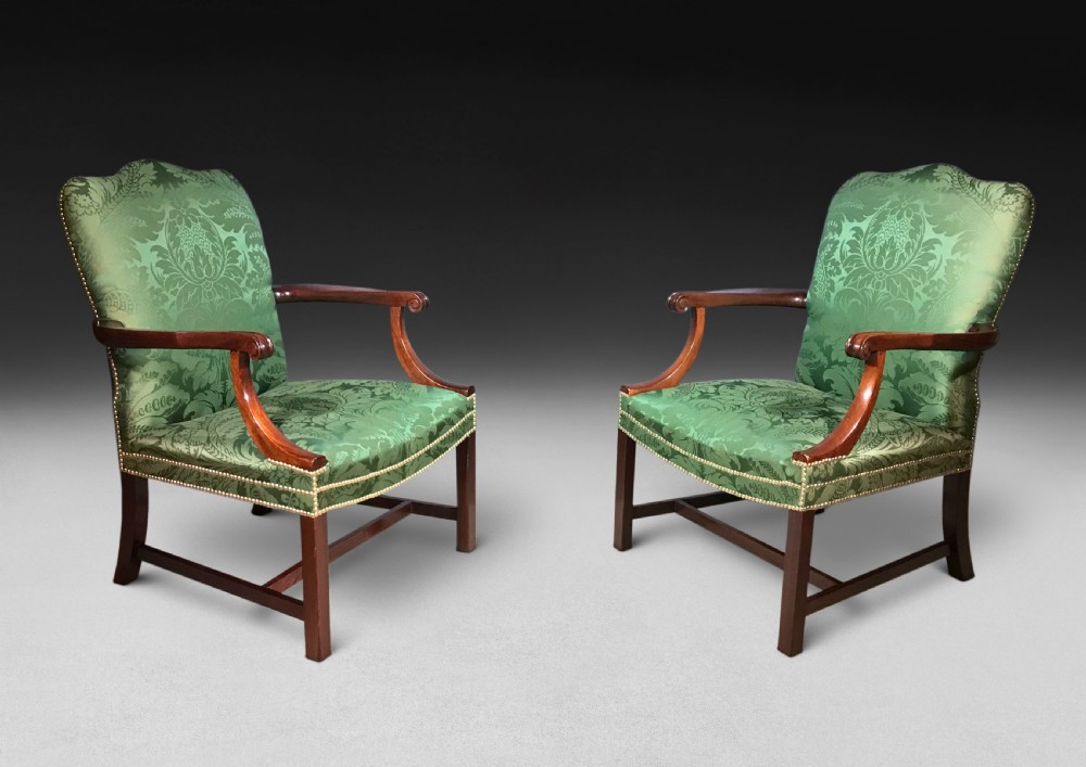 A pair of Chippendale period Gainsborough armchairs with carved mahogany frames, scrolled arms, and green damask upholstery trimmed with brass studs.