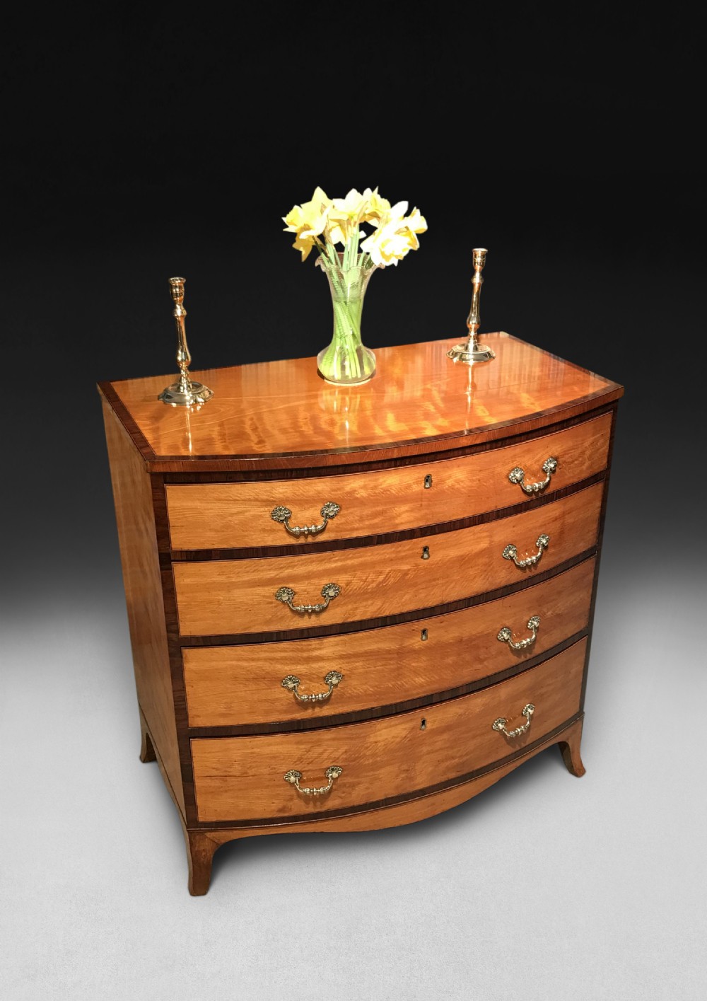 A George III period bowfront satinwood chest of drawers featuring kingwood crossbanding and four graduated drawers on bracket feet.