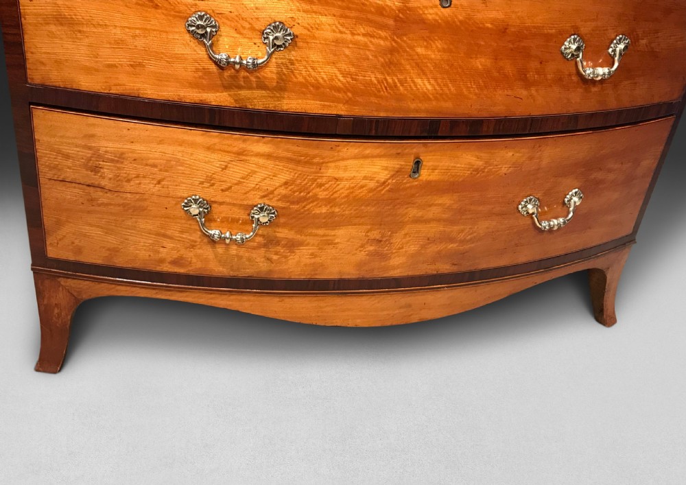 A George III period bowfront satinwood chest of drawers featuring kingwood crossbanding and four graduated drawers on bracket feet. View II