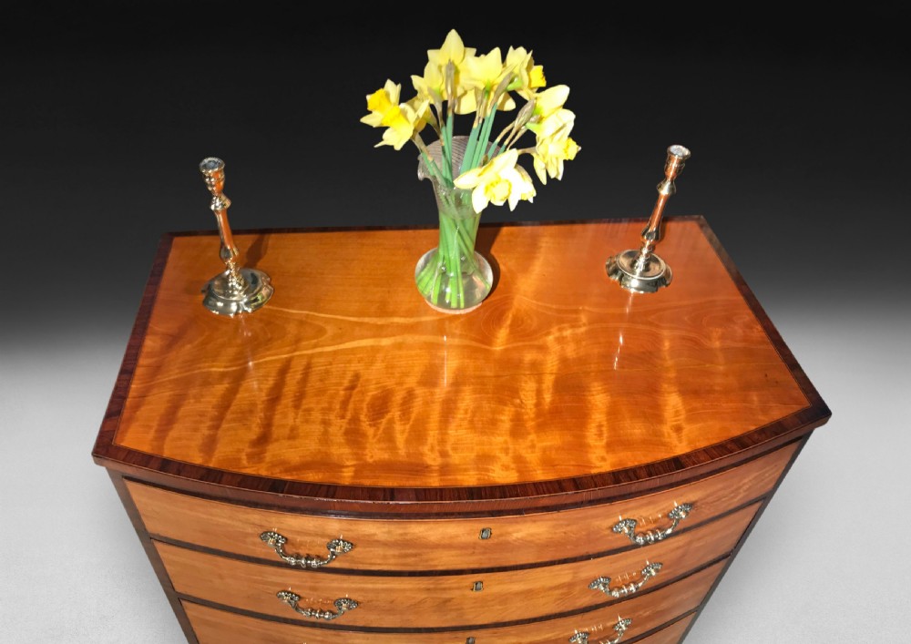 A George III period bowfront satinwood chest of drawers featuring kingwood crossbanding and four graduated drawers on bracket feet. View VIII