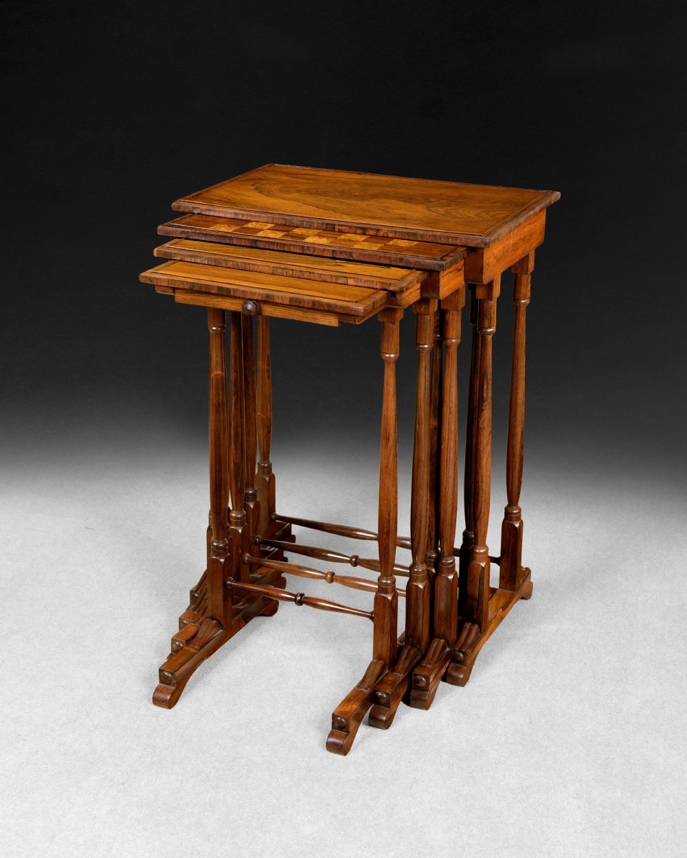 A set of four nested Regency rosewood quartetto tables featuring turned spindle legs, twin-ring stretchers, and an inlaid chessboard on the second surface.