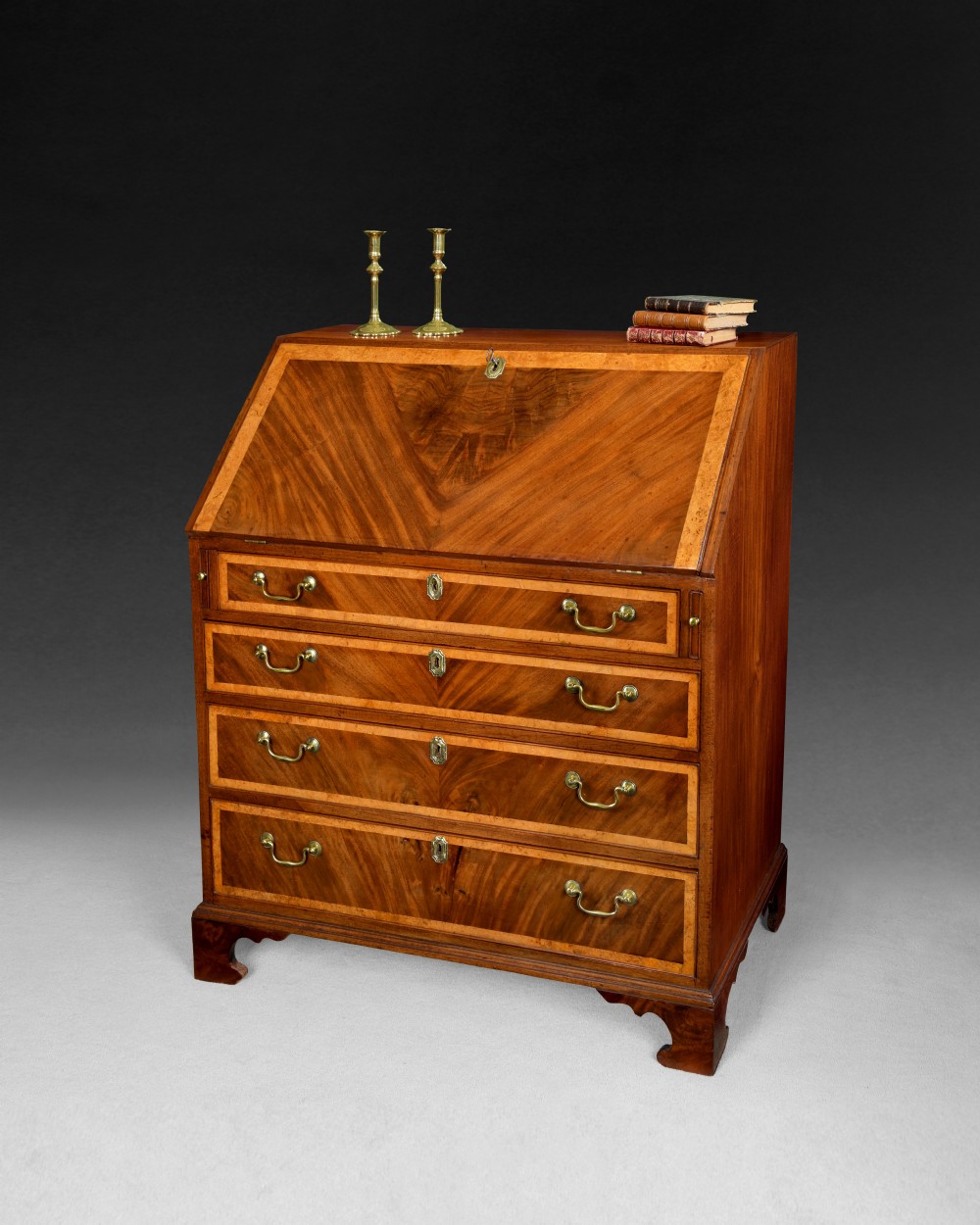 A George III flame mahogany slant-front writing bureau featuring burr yewwood crossbanded borders, four graduated drawers with brass handles, and bracket feet.