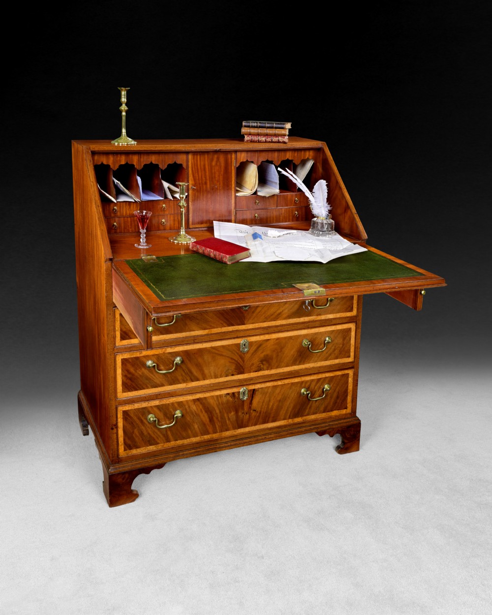 A George III flame mahogany slant-front writing bureau featuring burr yewwood crossbanded borders, four graduated drawers with brass handles, and bracket feet. View II