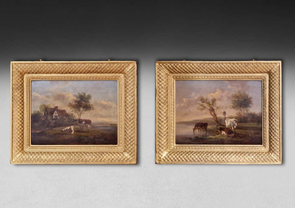 A pair of early 19th-century pastoral oil paintings depicting rural landscapes with grazing cattle, housed within matching decorative gilded frames.