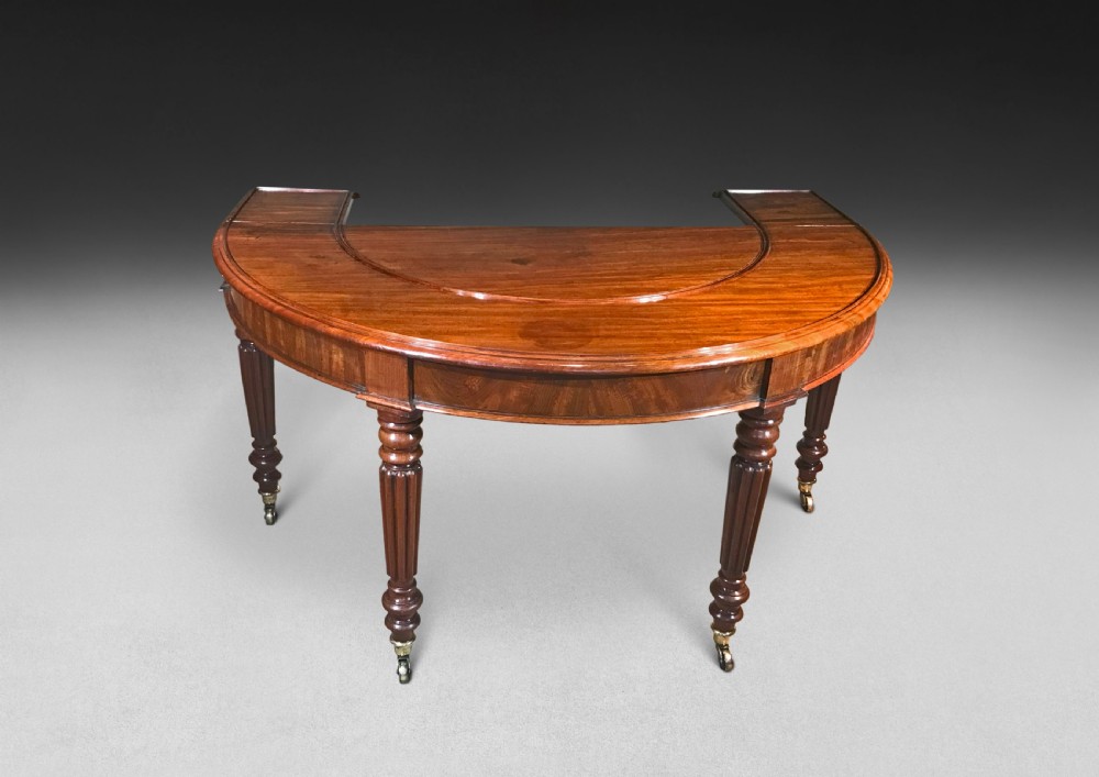 A horseshoe-shaped Regency mahogany hunt table featuring reeded turned legs with brass castors.