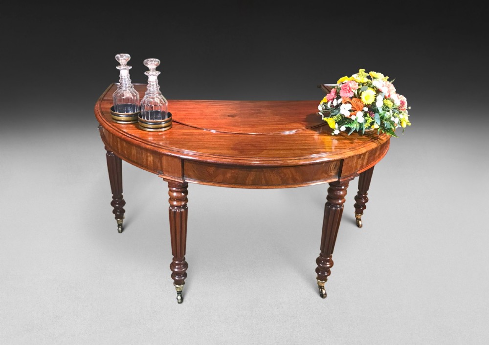 A horseshoe-shaped Regency mahogany hunt table featuring reeded turned legs with brass castors. View II