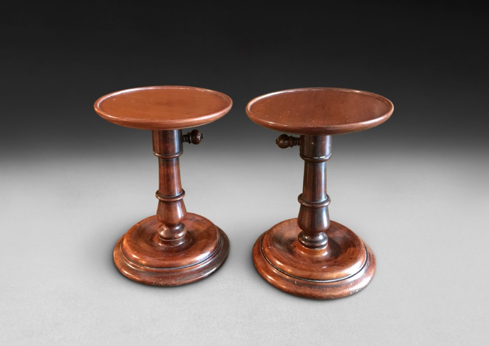 A pair of turned Georgian mahogany adjustable candle stands featuring circular dish tops and moulded round bases.