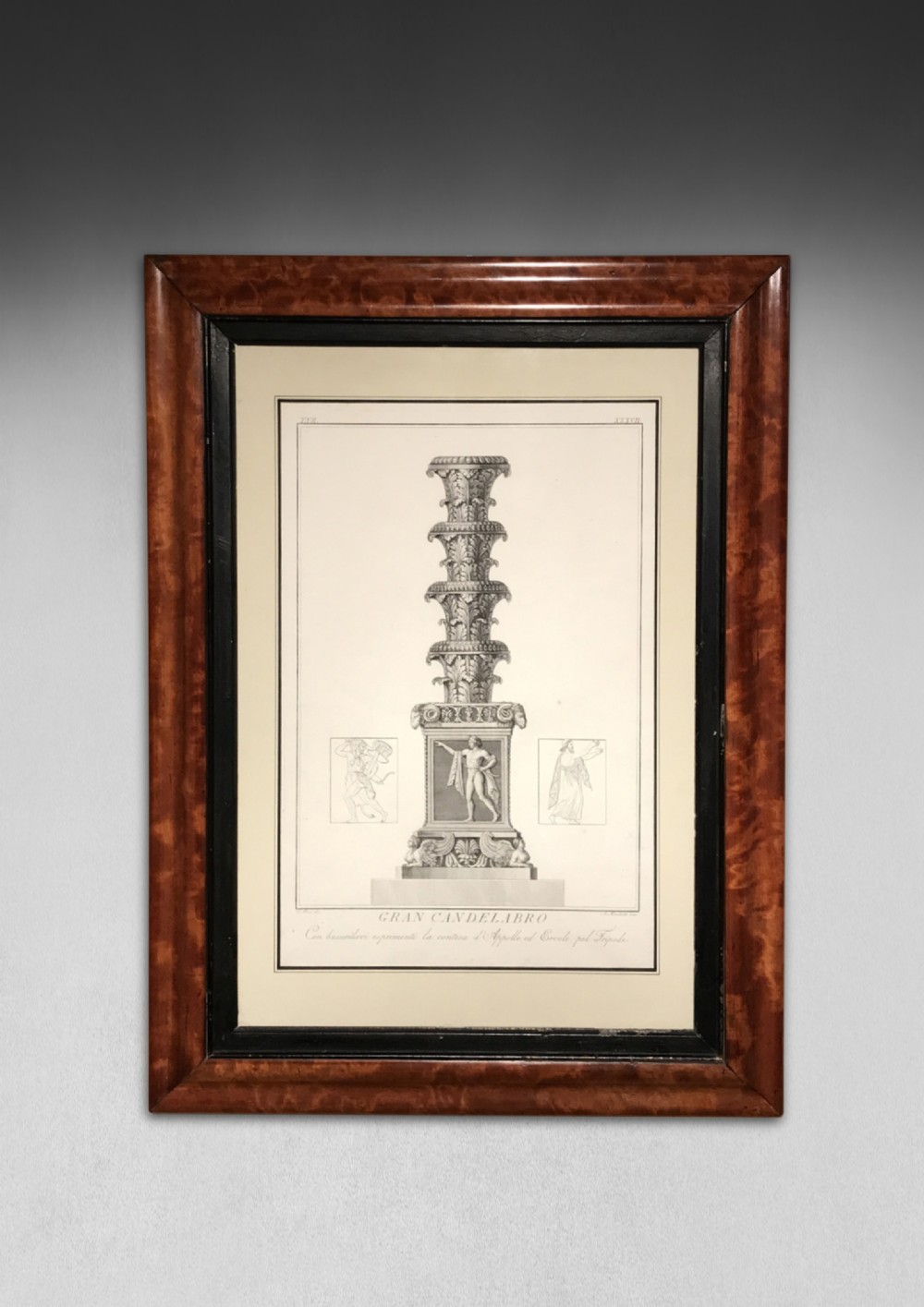 A framed Neoclassical copper engraving depicting a classical architectural candelabro printed on cream paper within a burl wood veneer frame.