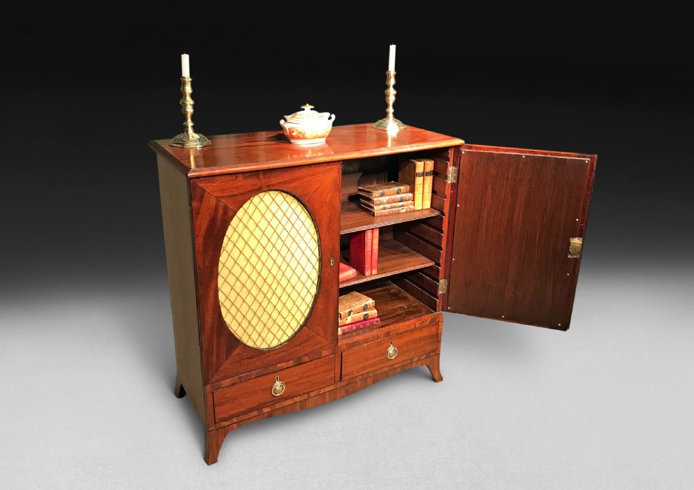 A George III mahogany side cabinet featuring two doors with oval brass wire grille panels above two short drawers, resting on bracket feet. View II