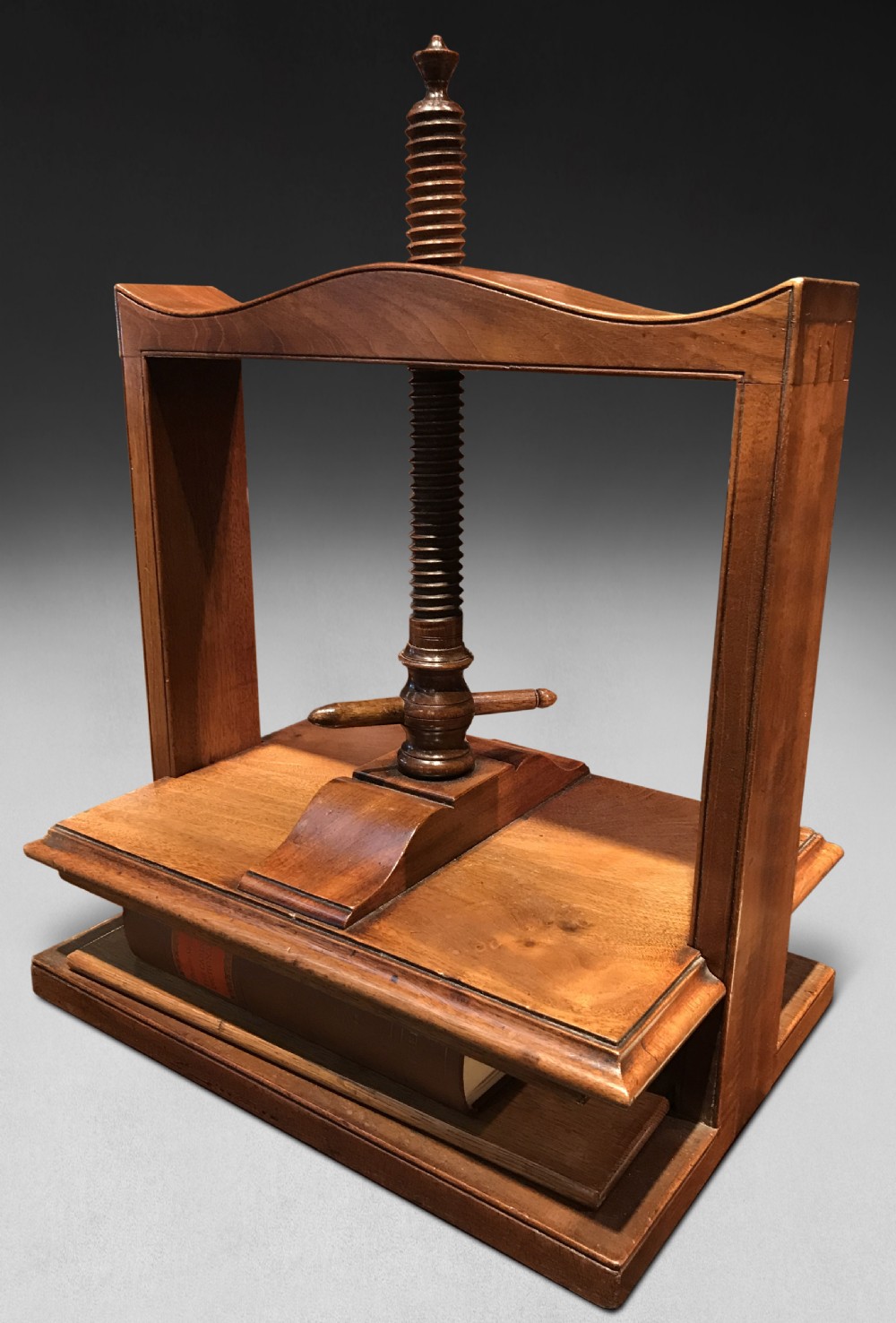 A George IV mahogany desktop book press featuring a central vertical wooden screw, turned handle, arched top rail, and flat base platform.