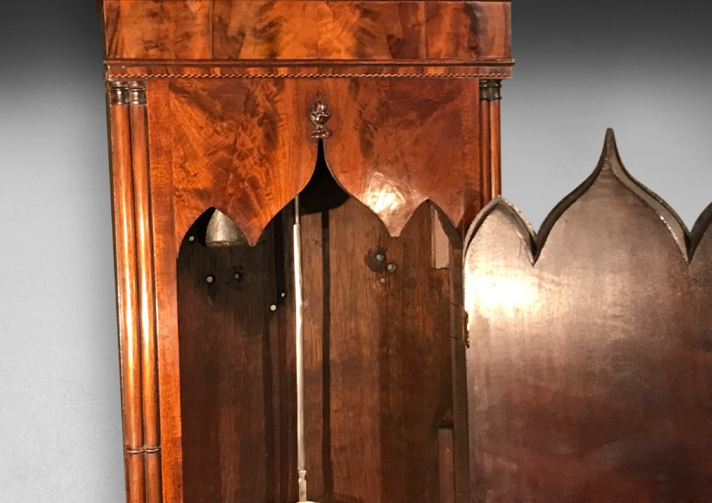 A George III mahogany longcase clock featuring a swan-neck pediment with brass eagle finial, an arched dial, and a flame mahogany trunk door. View II
