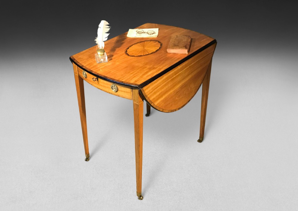 An 18th-century George III oval satinwood Pembroke table featuring rosewood crossbanding, a central elliptical marquetry medallion, a single front drawer with brass pulls, and tapered legs on brass castors. View II