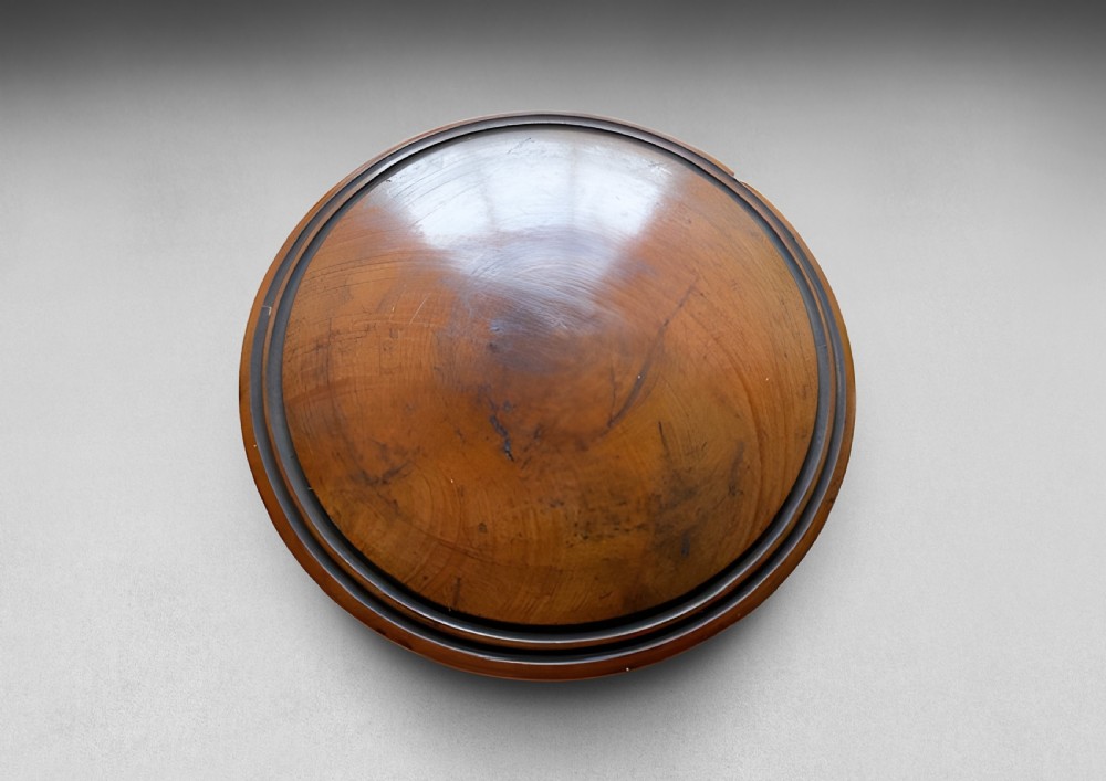 A circular turned wood case with a domed lid and concentric outer rings in a warm brown polished finish.